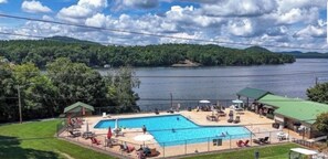 A swimming pool with lounge chairs, a covered area, and a view of a lake and forested hills.