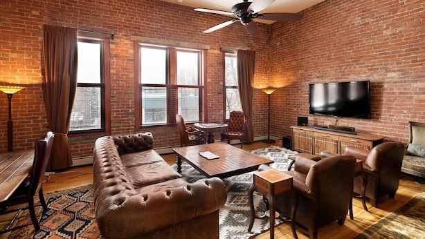 A living room with a brick wall, a ceiling fan, a flat-screen TV, leather furniture, and a patterned rug. - Remodeled Penthouse in the heart of Downtown Basalt, historic 1900's Building  (Basalt)