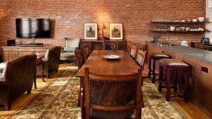A dining area with a brick wall, a flat-screen TV, wooden furniture, and a bar counter. - Remodeled Penthouse in the heart of Downtown Basalt, historic 1900's Building  (Basalt)