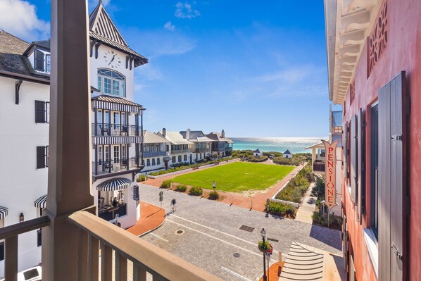 A view from a balcony overlooking a courtyard with a lawn, a clock tower, and a building with a 'Pension' sign.