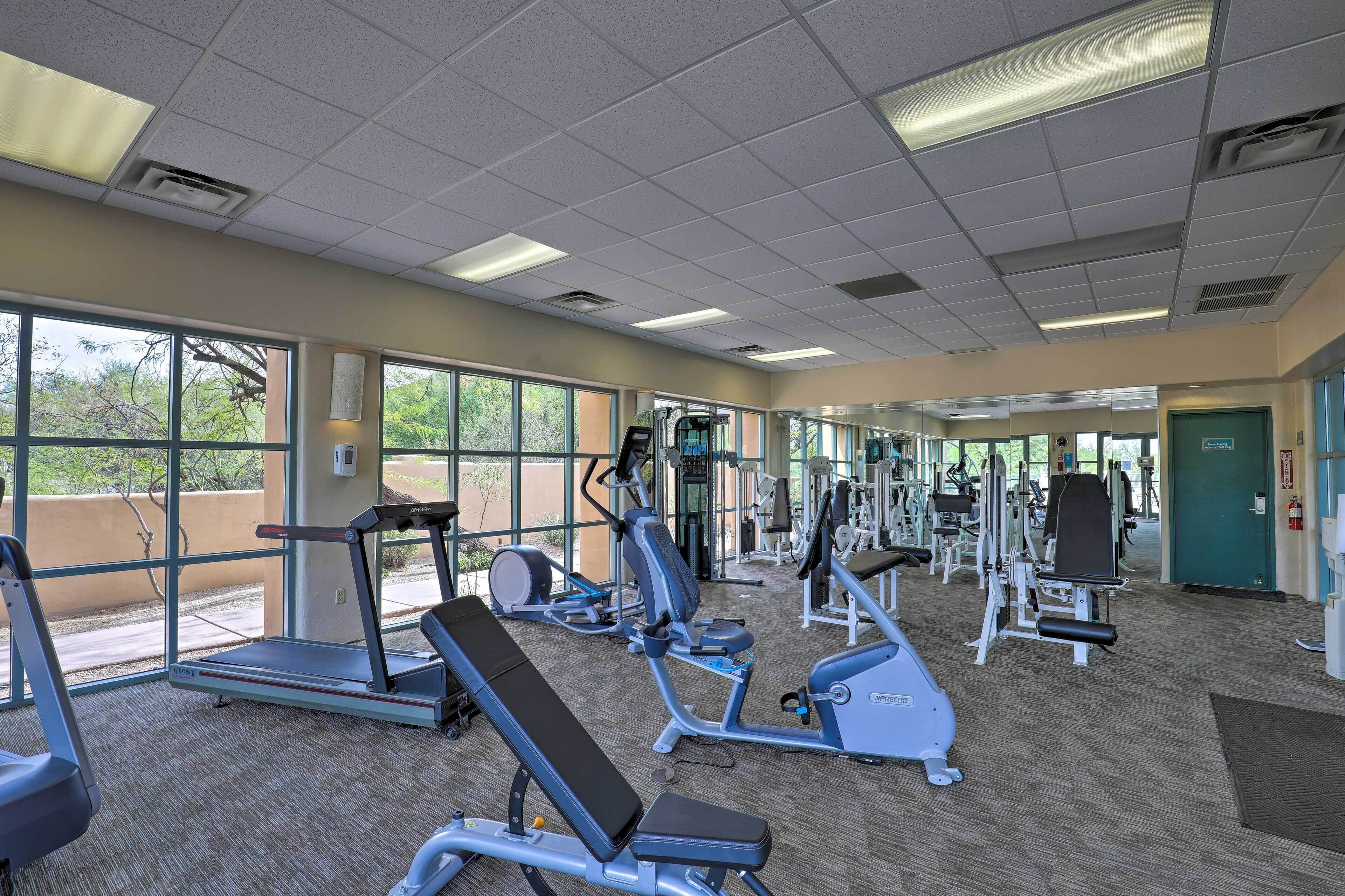 Ein Fitnessstudio mit unterschiedlichen Trainingsgeräten, großen Fenstern und einem Teppichboden.
