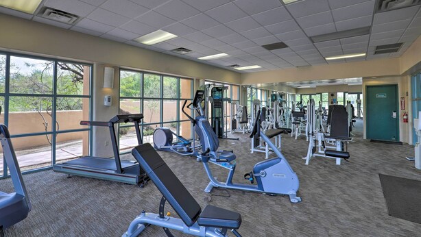 Ein Fitnessstudio mit unterschiedlichen Trainingsgeräten, großen Fenstern und einem Teppichboden.