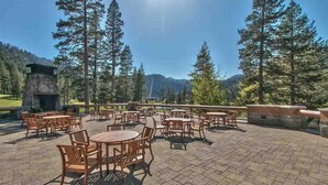 Une terrasse extérieure avec des tables et des chaises rondes, entourée de grands arbres et dominée par un paysage montagneux.