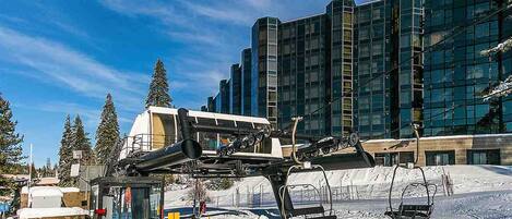 A ski lift with a chairlift system in a snowy area, a modern building with reflective glass windows, and a clear blue sky.