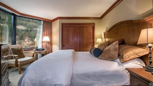 Une chambre d’hôtel avec un grand lit, une tête de lit en bois, un bureau avec une lampe, une chaise et une vue sur l’extérieur par une grande fenêtre.