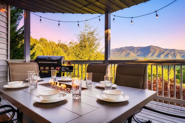 Un espace extérieur abrité, aménagé pour les repas, avec un barbecue, des sièges et une vue panoramique sur les montagnes.
