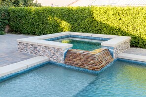 Et rektangulært swimmingpool med murstens- og flisekant, omgivet af en hæk og en belagt terrasse.
