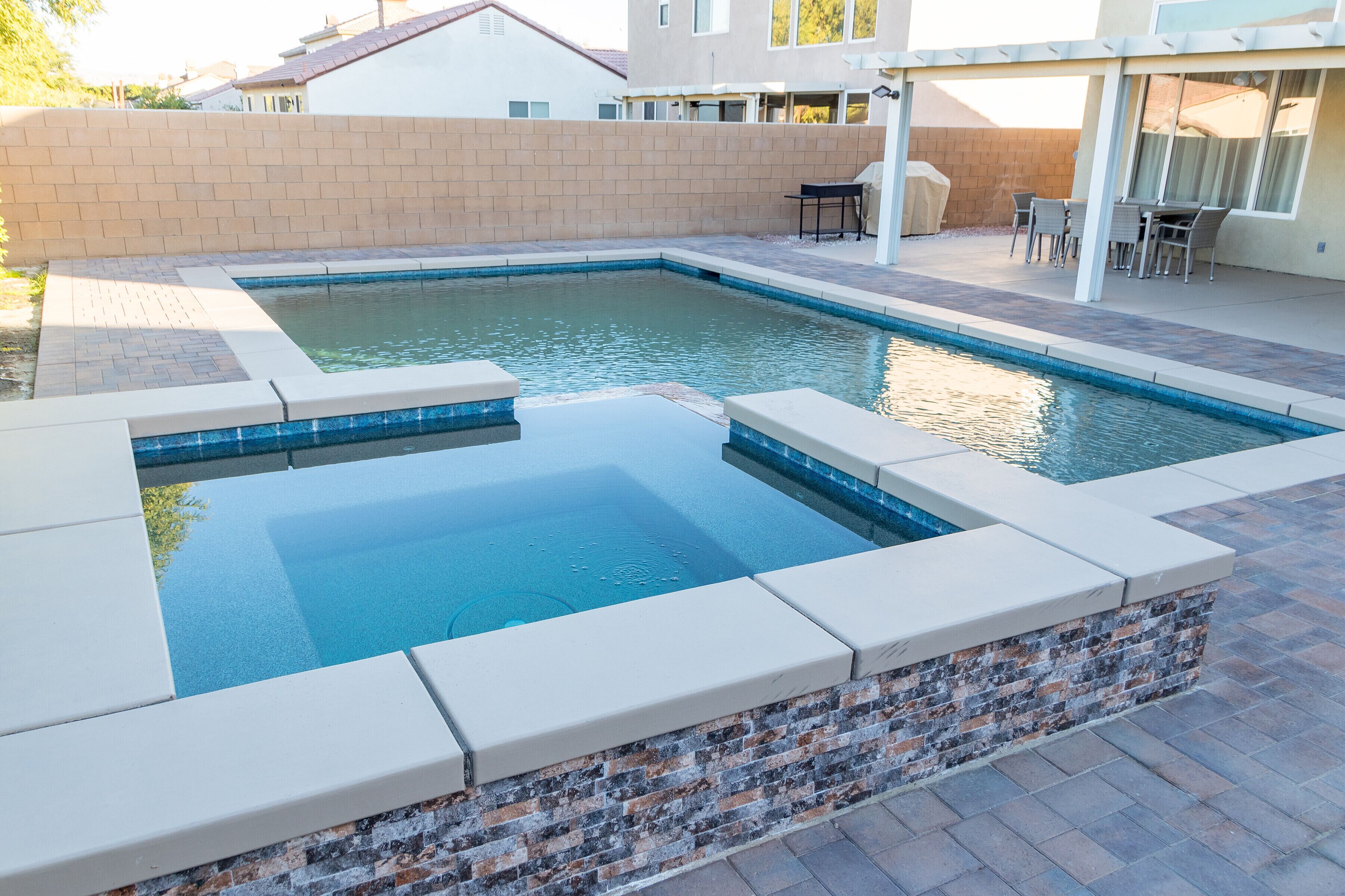 A rectangular swimming pool with a tiled edge and a brick accent wall.