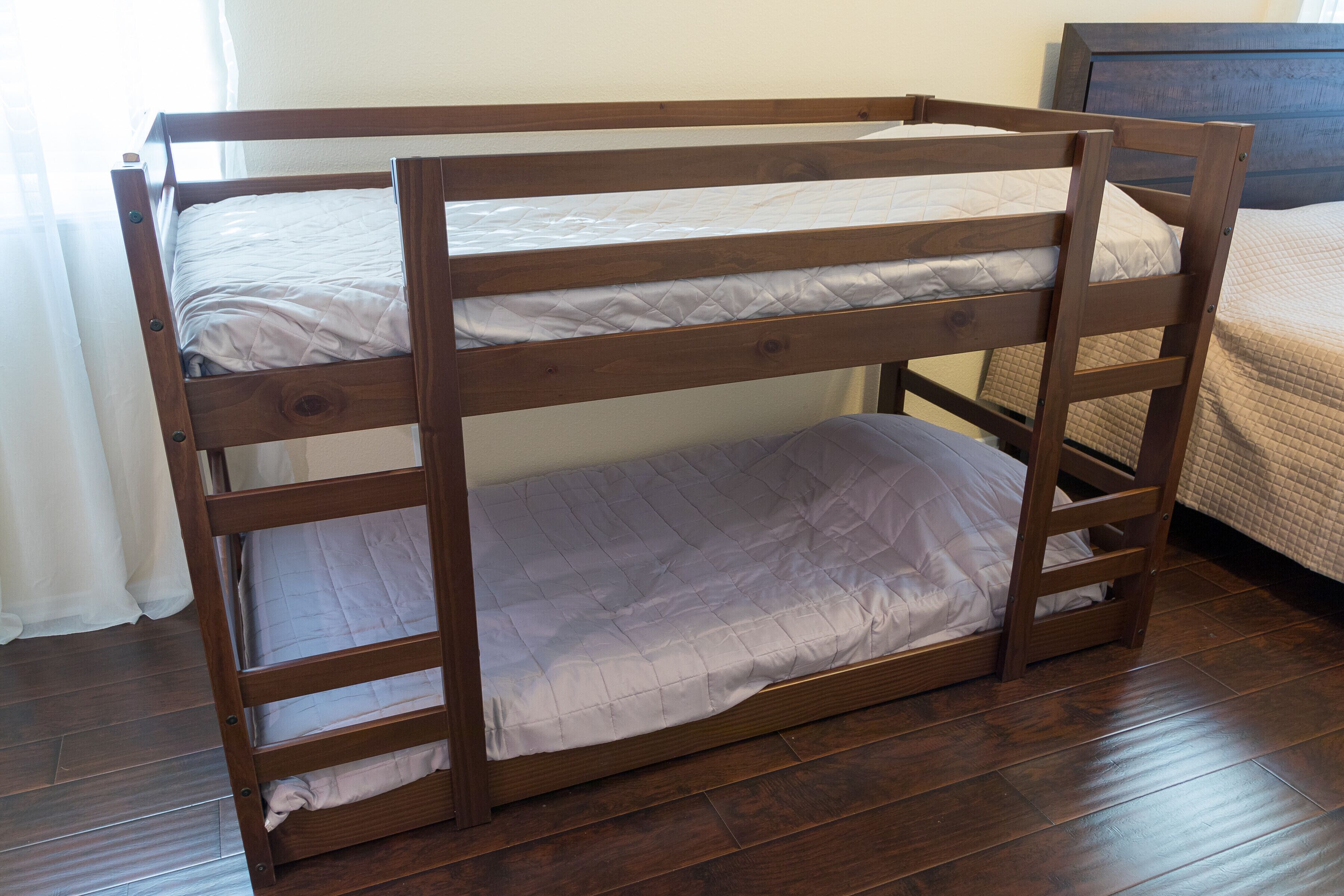 Een stapelbed met twee niveaus, houten frame en witte beddengoed.