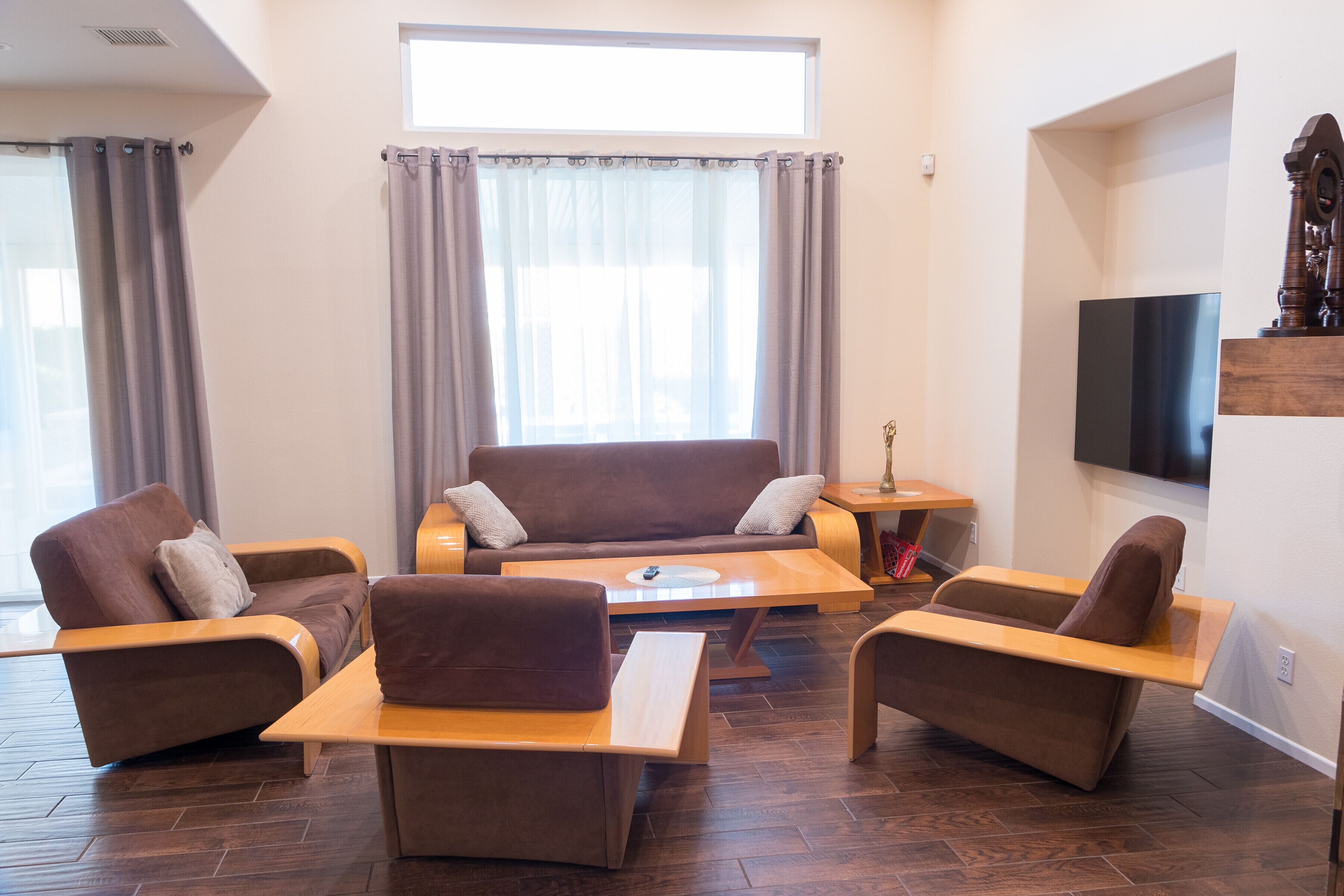 Een moderne woonkamer met een bruine bank, twee fauteuils, een salontafel en een flatscreen televisie aan de muur.