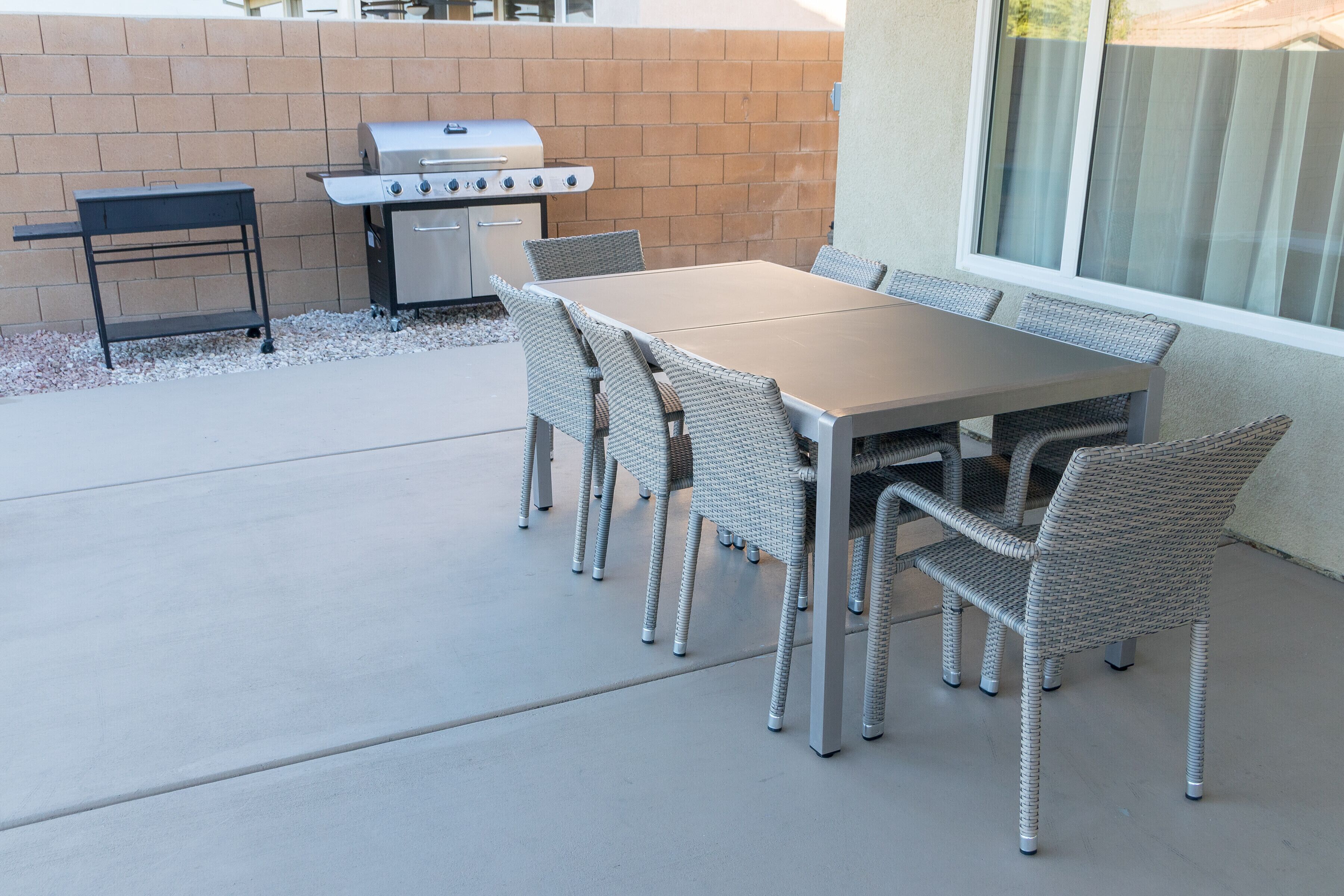 An outdoor patio with a barbecue grill, a table with chairs, and a window.
