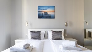 A hotel room with a large bed, two bedside tables, a painting of a sunset over a pier, and a mirror on the right wall. - Di Verdi Imperial Hotel (Budapest)