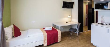 A hotel room with a bed, desk, chair, TV, and kitchenette.