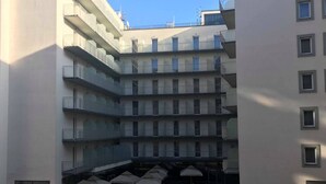 A multi-story residential building with balconies, a central courtyard with umbrellas, and a stairway leading to the upper floors. - Di Verdi Imperial Hotel (Budapest)