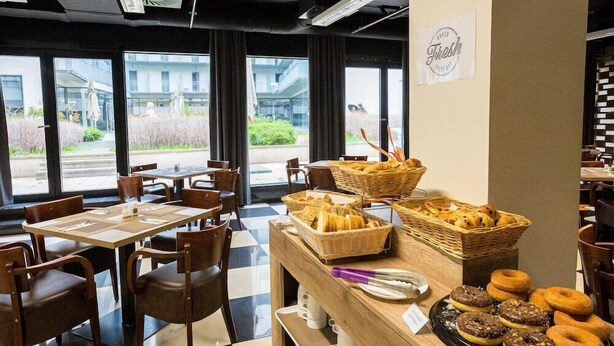 A cafe with tables and chairs, a counter with baskets of bread and pastries, and a sign that says "Fresh". - Di Verdi Imperial Hotel (Budapest)