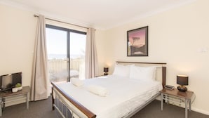 A hotel room with a large bed, a TV, a bedside table, and a window with curtains. - Alaska - 8 Poley Cow Lane (Jindabyne)