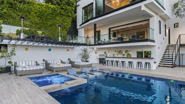 Ett modernt hus i två våningar med en swimmingpool, en uteplats och en bar.