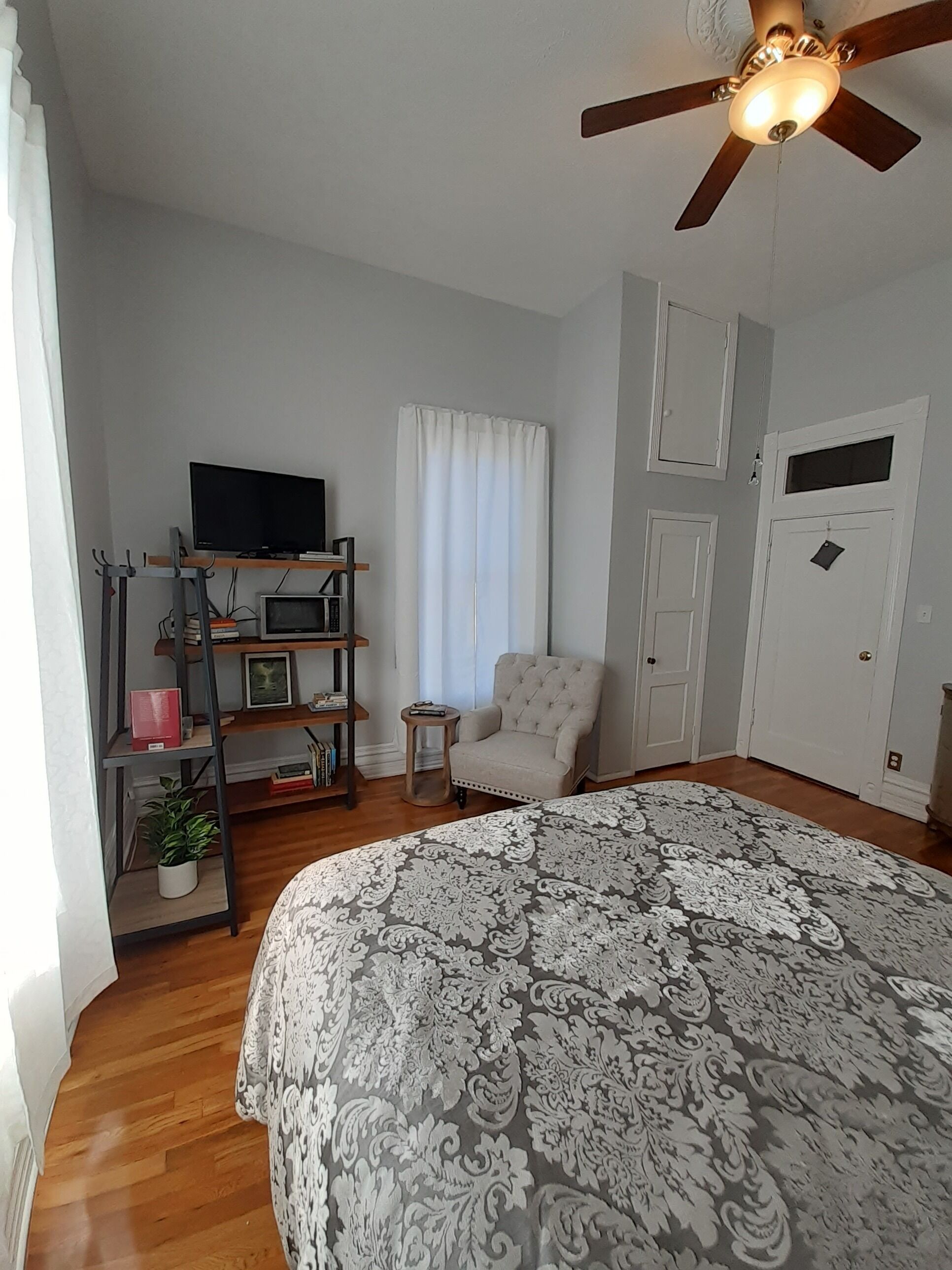 A bedroom with a large bed, a ceiling fan, a TV, a bookshelf, and a chair.