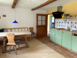 Una cocina con una mesa de madera, sillas, una lámpara azul colgante, un mueble verde y un salpicadero de azulejos.