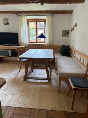 Una habitación acogedora con una mesa de madera, un sofá, un televisor y una ventana con cortinas.
