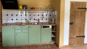 Eine Küche mit Spüle, grünen Schränken, einer Holztür und einer gefliesten Spritzschutzwand.