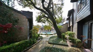 Un barrio residencial con un sendero estrecho, casas de ladrillo y un árbol grande.