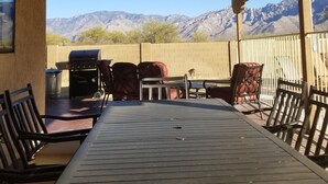 Een terras buiten met een houten tafel en stoelen, een barbecue en uitzicht op bergen.