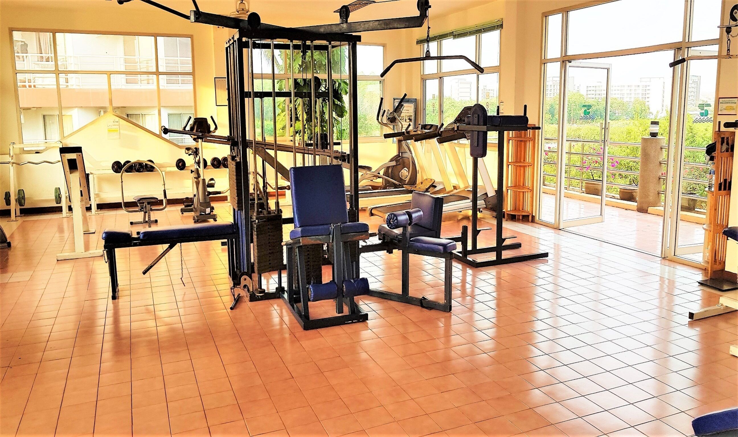 Ett gym med olika typer av träningsutrustning, stora fönster och ett klinkergolv.