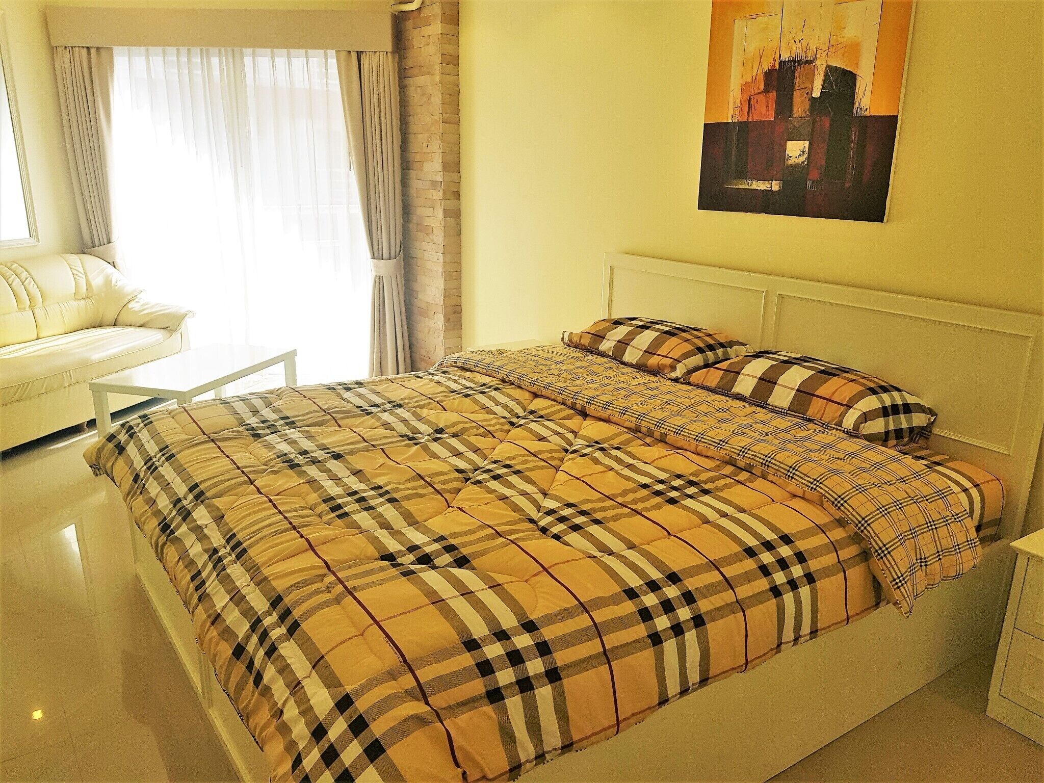 Un dormitorio con cama, cabecera blanca, un cuadro en la pared y ventana con cortinas.