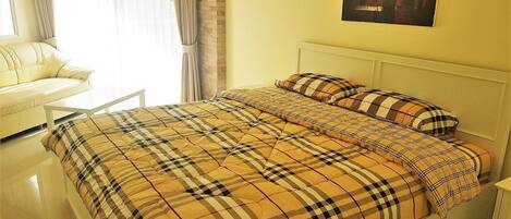 Un dormitorio con cama, cabecera blanca, un cuadro en la pared y ventana con cortinas.