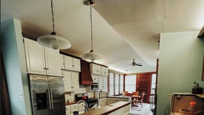 Una cocina con isla central, armarios blancos, electrodomésticos de acero inoxidable e iluminación colgante.