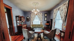 Una habitación con un sofá verde, dos sillones, una mesa de centro de madera y una araña.