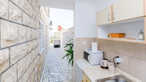 A narrow stone-walled kitchen with a stone floor, a microwave, a kettle, and a sink. - Rooms Nikola (Dubrovnik)