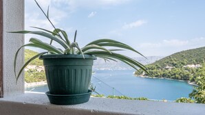Ein Blumentopf auf einem Balkon mit Blick auf die Küste, eine Brücke und Hügel.