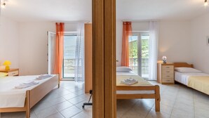 Ein Hotelzimmer mit zwei Betten, Holzboden, einem Balkon mit Vorhängen und Blick ins Grüne.