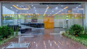A modern reception area with glass doors, a staircase, and indoor plants. - Hotel Royal Suites (Kolar)