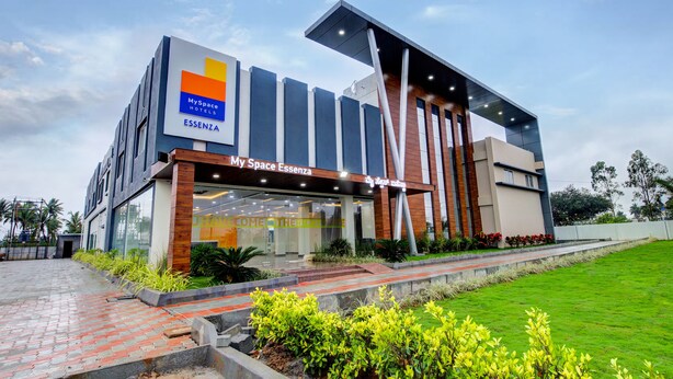 A modern MySpace hotel with a prominent entrance, large windows, and a well-maintained garden area. - Hotel Royal Suites (Kolar)