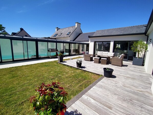 Eine moderne Außenpatio mit Holzterrasse, Gartenmöbeln und einem Pool mit Glasverkleidung.