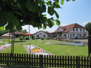 A park with a playground, a building with a red roof, and a wooden fence.