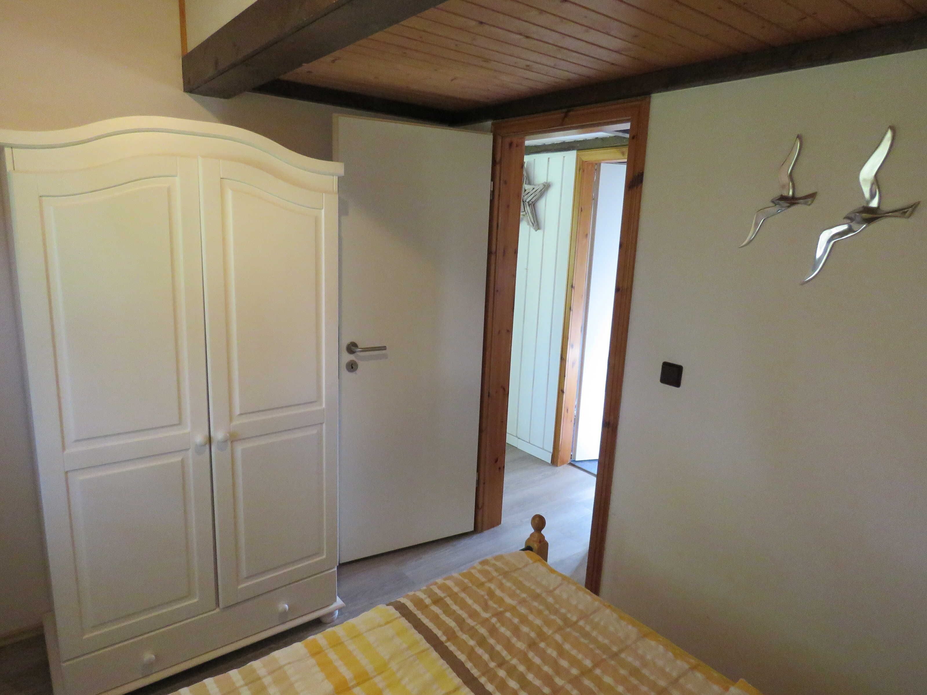 A bedroom with a large wardrobe, a bed with a checkered bedspread, and a wooden ceiling.