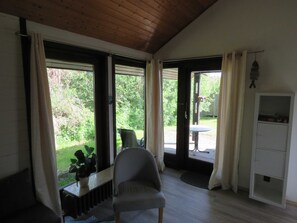 A room with a wooden ceiling, a chair, a small table with a plant, and a cabinet.
