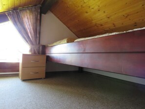 Una camera da letto con soffitto in legno, un letto, un comodino e una finestra con tende.