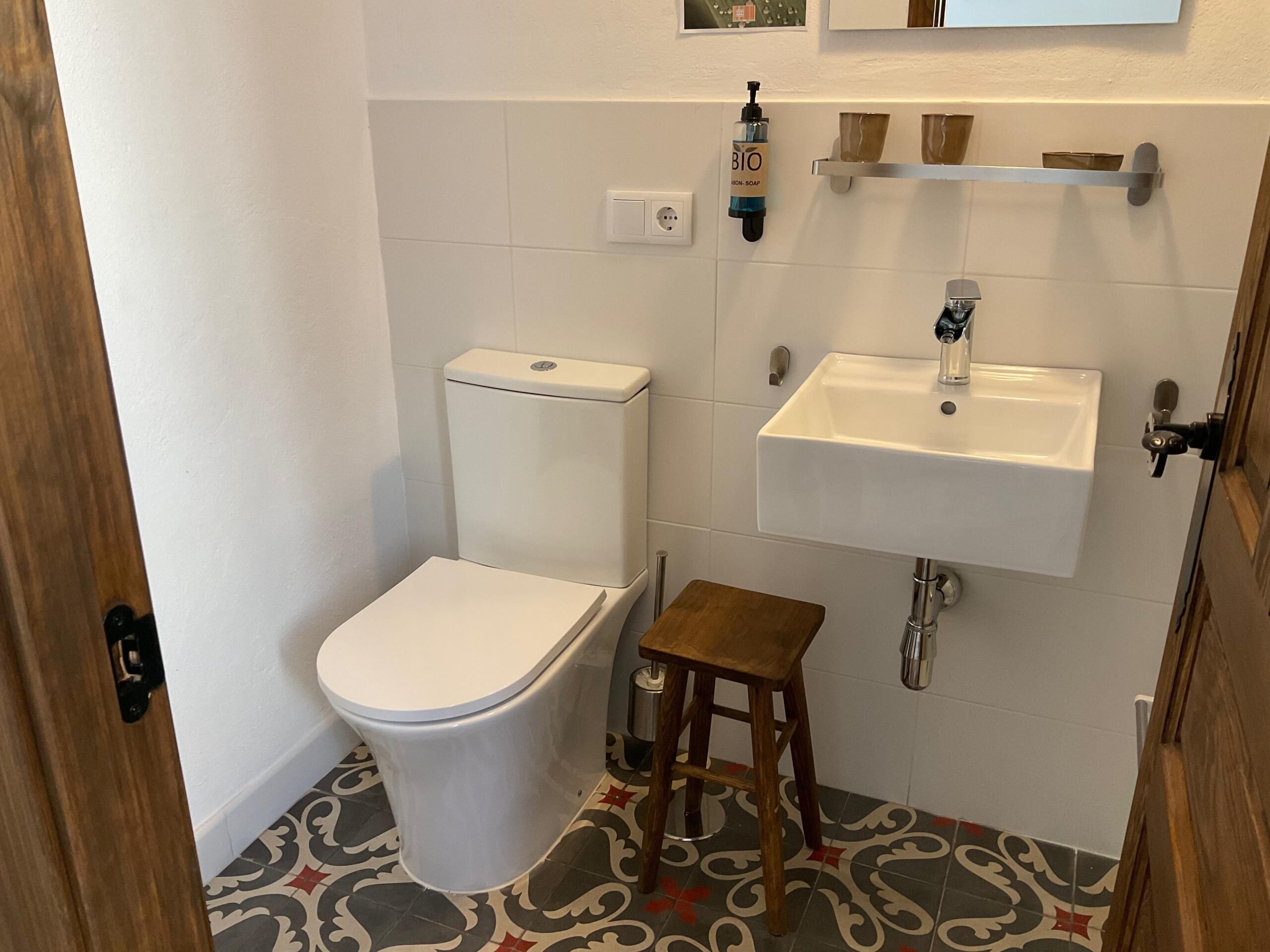 Un baño pequeño con inodoro, lavamanos y un taburete.