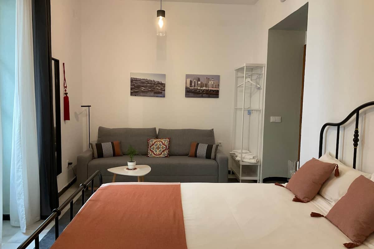 Una habitación de hotel con cama, sofá, una mesita y perchero.