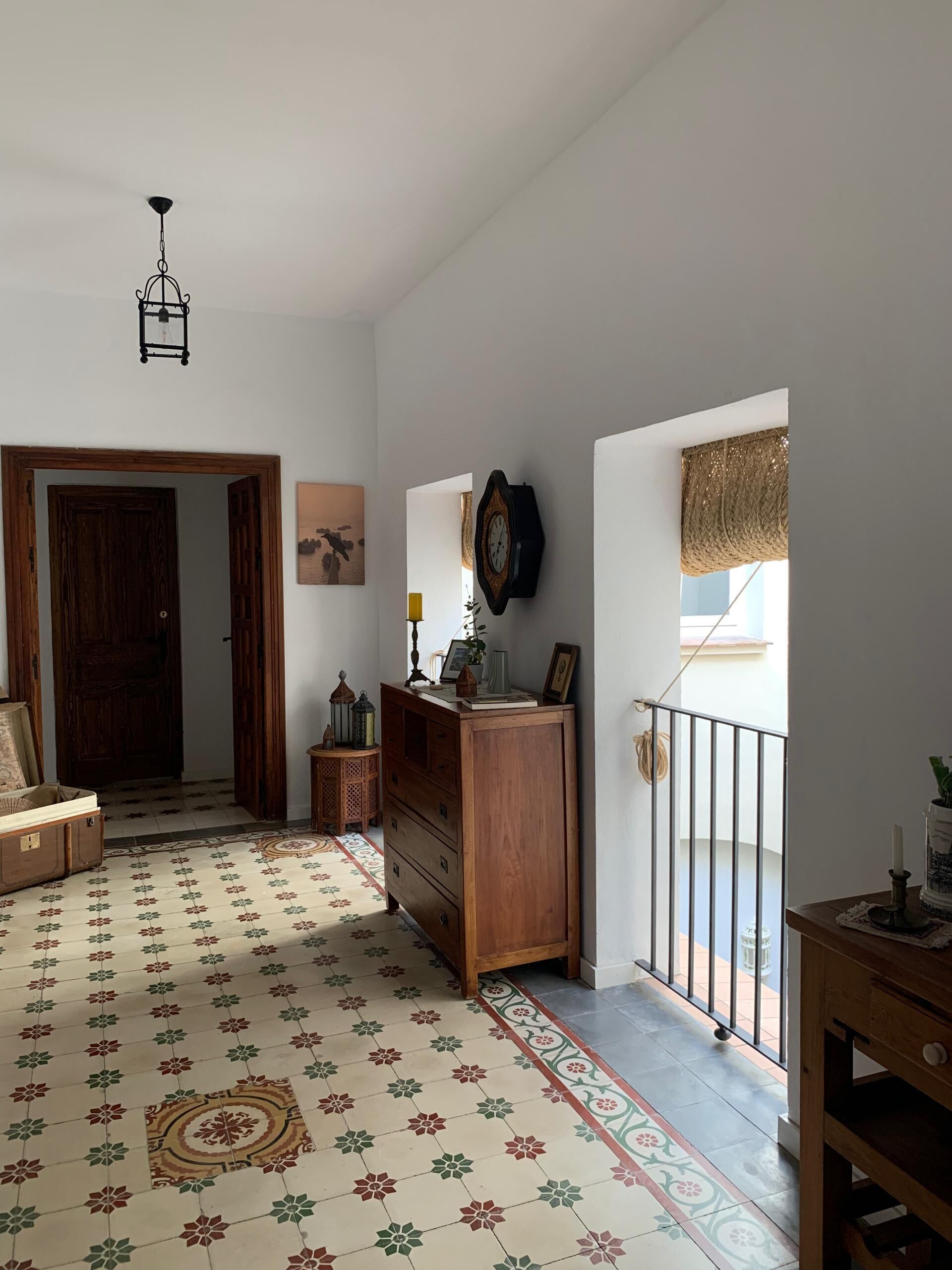 Um corredor amplo com piso estampado, uma porta de madeira, um aparador e um relógio fixado na parede.
