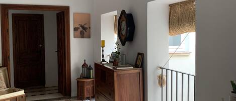 Um corredor amplo com piso estampado, uma porta de madeira, um aparador e um relógio fixado na parede.