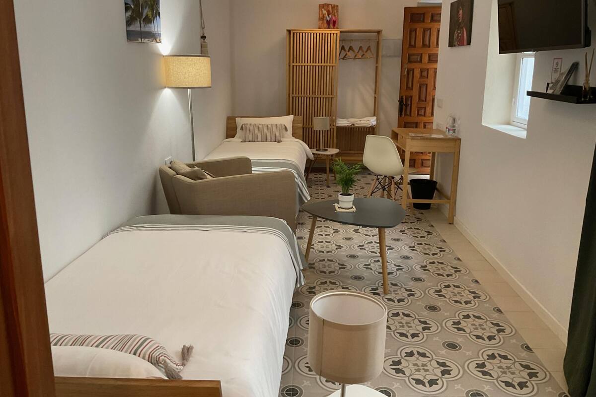 Habitación de hotel pequeña con dos camas, un escritorio, una silla, una mesita y un televisor montado en la pared.