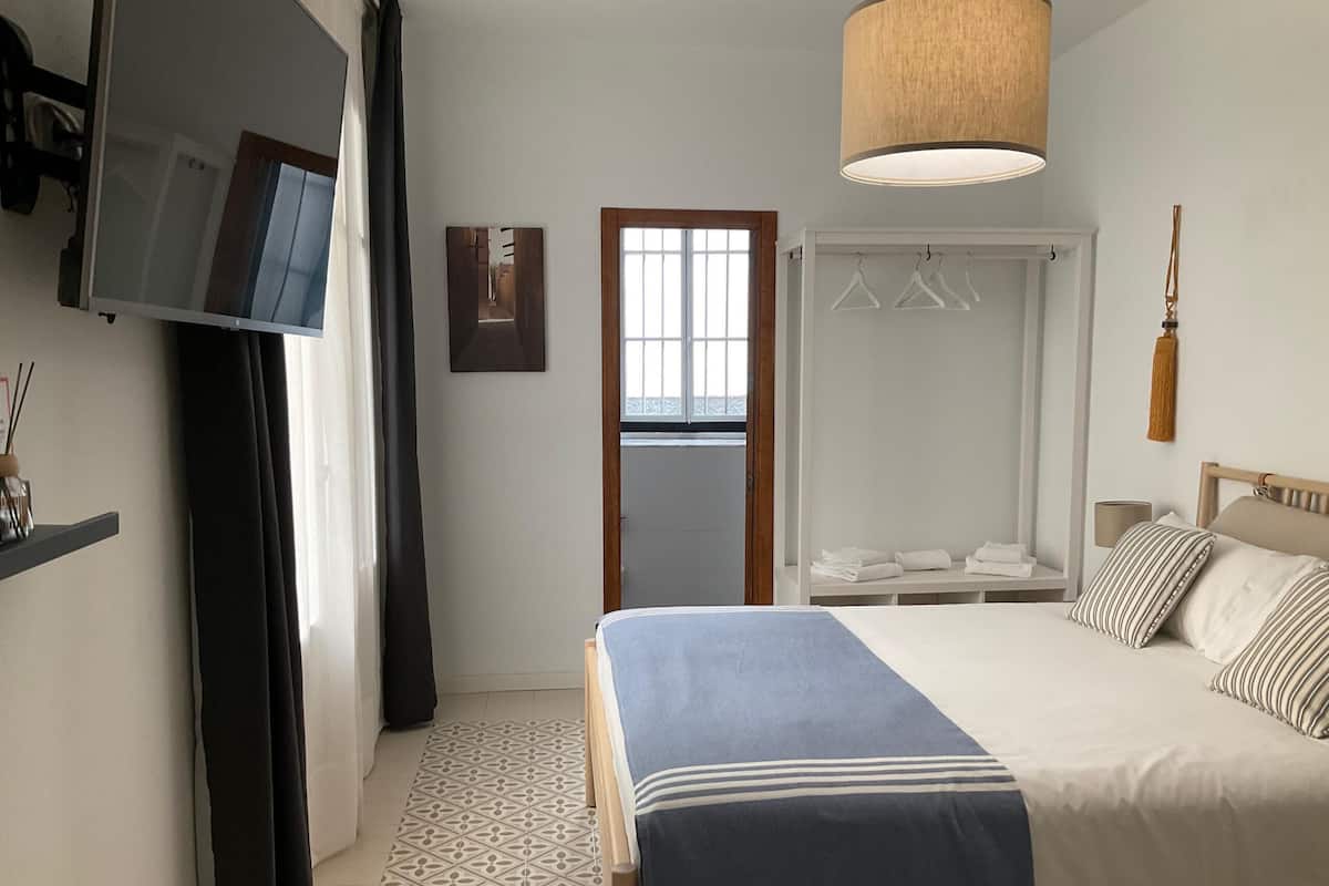 Una habitación de hotel con cama, televisión, armario y lámpara colgante.