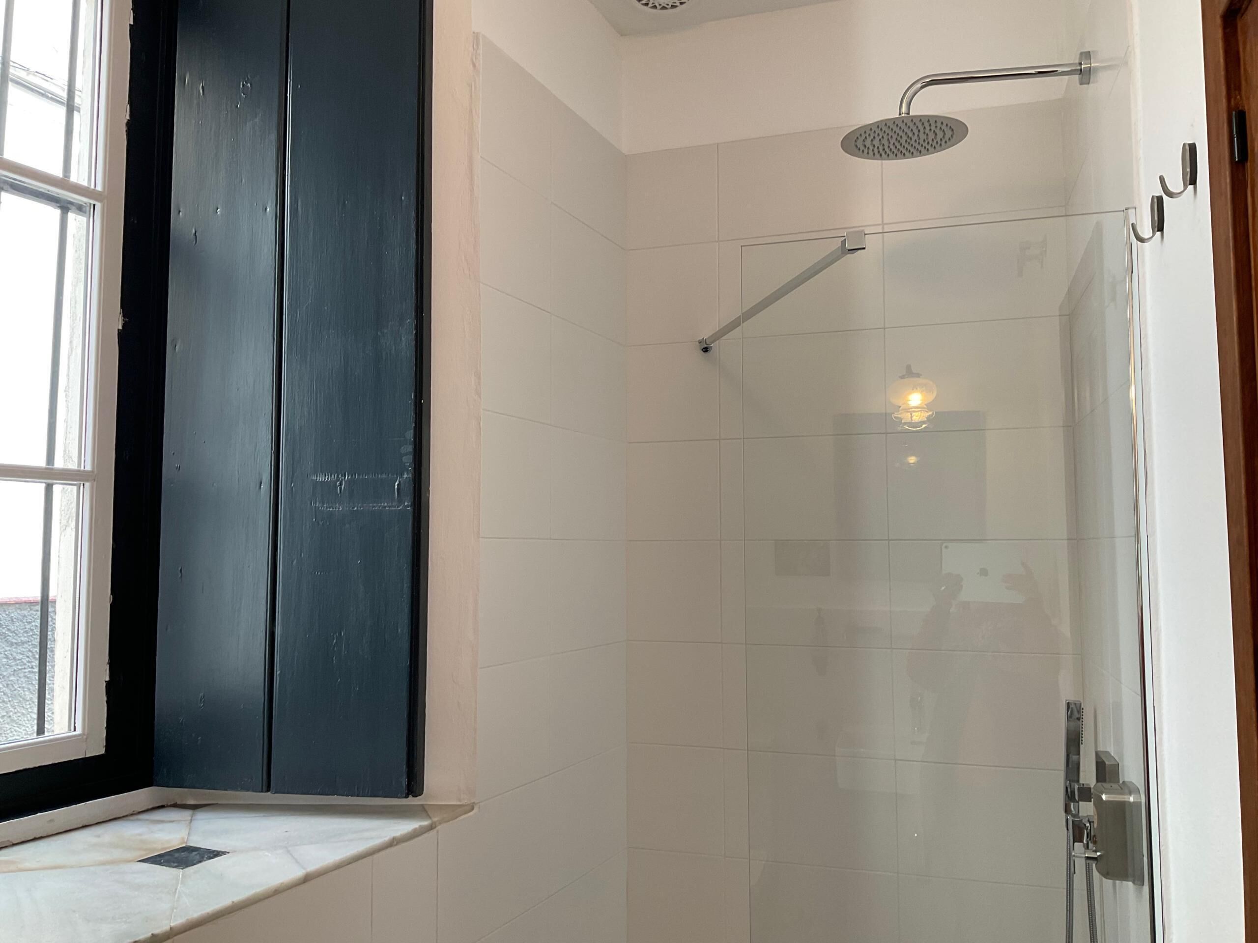 Ein modernes Badezimmer mit Duschkabine aus Glas, einem großen Fenster und einer dunklen Holztür.