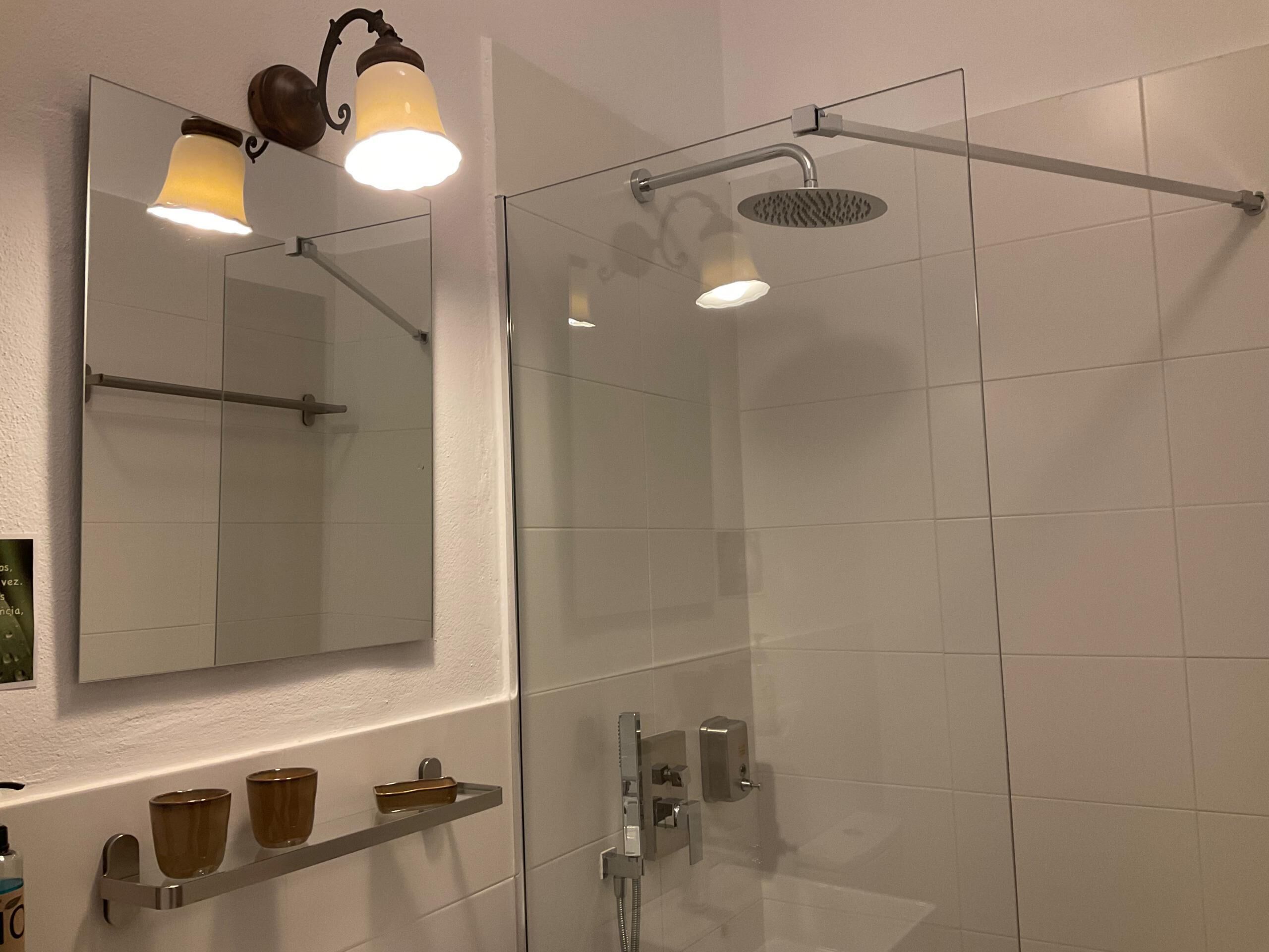 Un baño moderno con cabina de ducha de vidrio, un espejo grande y un estante con artículos de aseo.
